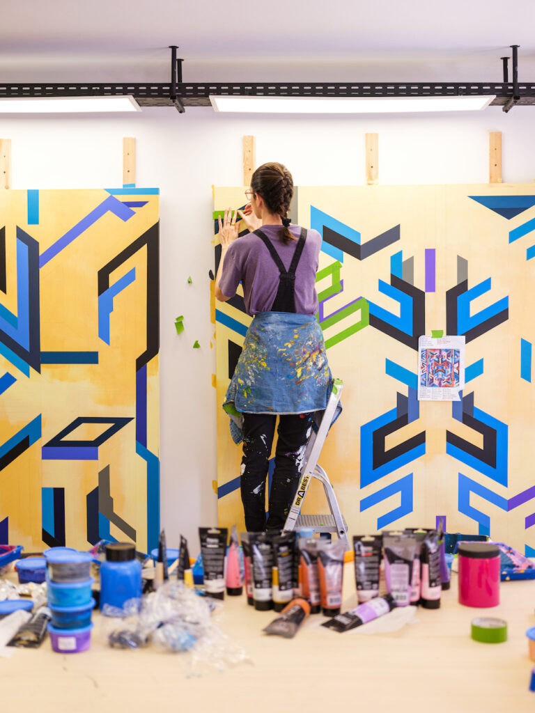 Moroccan visual artist Ghizlane Agzenaï standing in her studio beside colorful geometric totem artworks