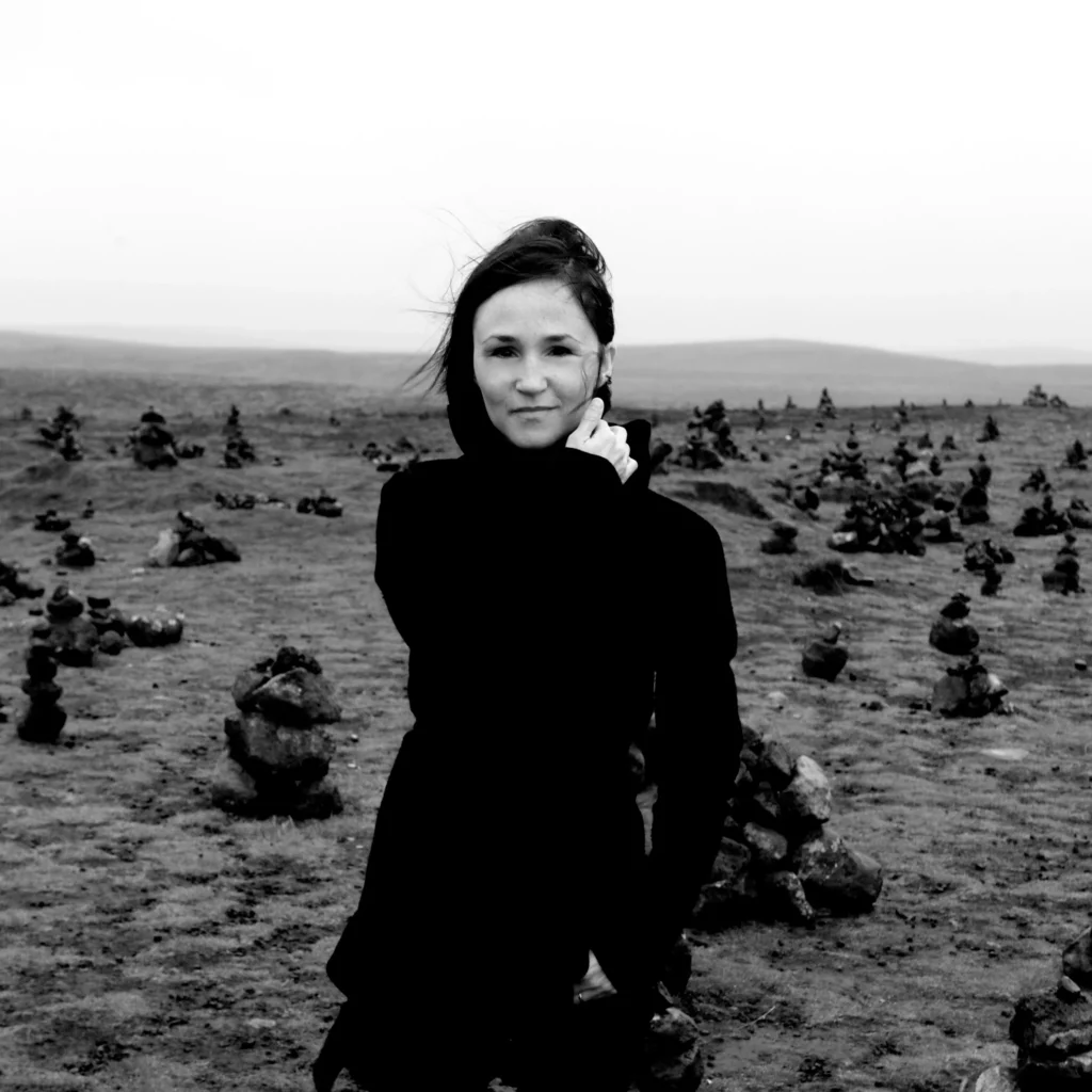 Black-and-white outdoor portrait of Icelandic composer Anna Thorvaldsdottir among low stone cairns, photographed by Saga Sigurdardottir.