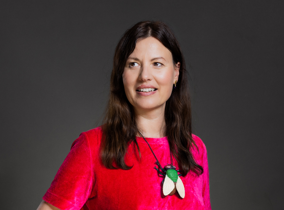 Portrait of Czech writer Dora Kaprálová in a bright pink top against a dark grey background, photographed by Connor Jandourek Photostudio
