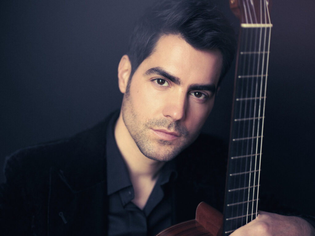 Portrait of Montenegrin guitarist Miloš Karadaglić seated with a classical guitar